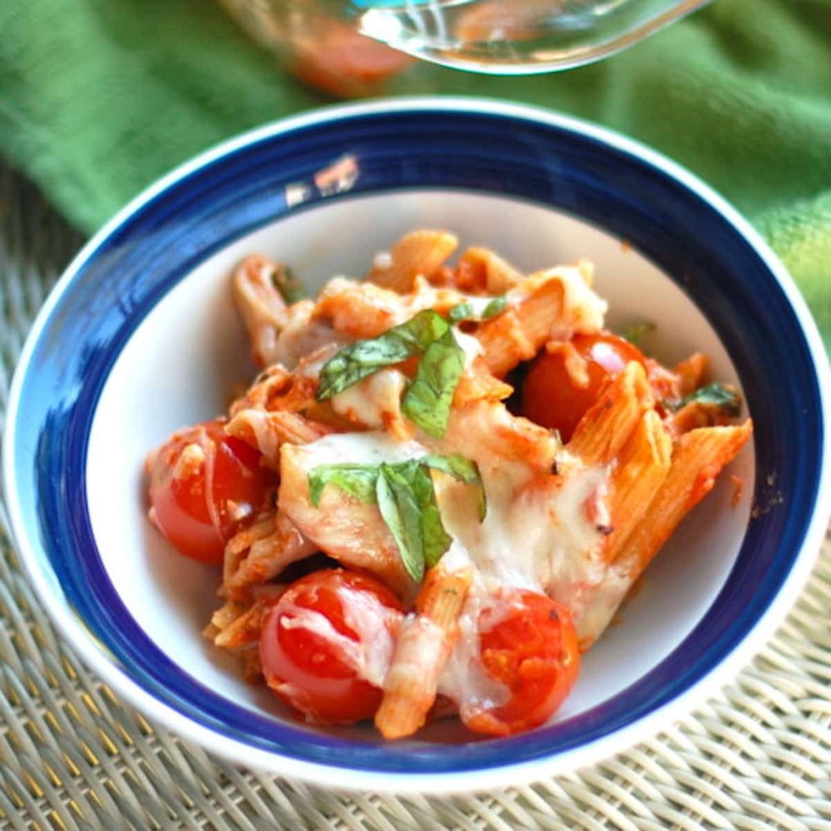 Vegetarian caprese penne pasta with sweet cherry tomatoes, mozzarella, and fresh basil in a bowl.