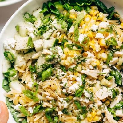Hand holding Orzo Summer Salad in a bowl with fork.